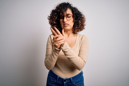 Young beautiful curly arab woman wearing casual t-shirt and glasses over white background Suffering pain on hands and fingers, arthritis inflammation