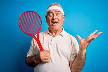 Middle age hoary sportsman playing tennis using racket over isolated blue background very happy and excited, winner expression celebrating victory screaming with big smile and raised hands