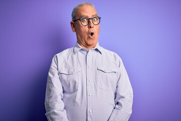 Middle age handsome hoary man wearing striped shirt and glasses over purple background afraid and shocked with surprise expression, fear and excited face.