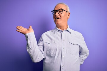 Middle age handsome hoary man wearing striped shirt and glasses over purple background smiling cheerful presenting and pointing with palm of hand looking at the camera.