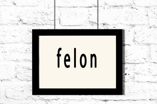 Black Frame Hanging On White Brick Wall With Inscription Felon