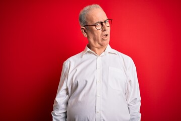 Middle age handsome hoary man wearing casual shirt and glasses over red background In shock face,...