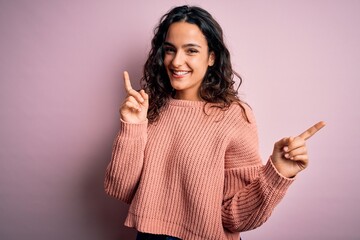 Young beautiful woman with curly hair wearing casual sweater over isolated pink background smiling confident pointing with fingers to different directions. Copy space for advertisement