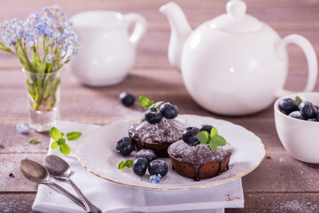 Chocolate cakes (cupcakes) are on the table. Cupcakes decorated  blueberries and green leaves mint on top. Beautiful and elegant serving with white dishes