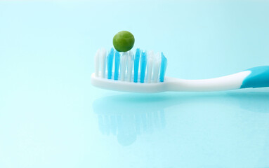 Fototapeta na wymiar A tooth brush on a hygienic background, with a green pea on it. People should use the size of a pea amount fluoride toothpaste on brush concept. Could be used for dental care education.