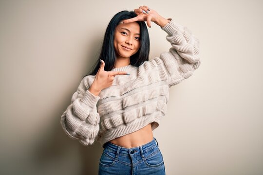 Young beautiful chinese woman wearing casual sweater over isolated white background smiling making frame with hands and fingers with happy face. Creativity and photography concept.