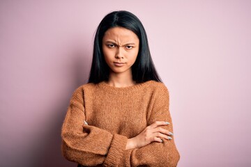 Young beautiful chinese woman wearing casual sweater over isolated pink background skeptic and nervous, disapproving expression on face with crossed arms. Negative person.