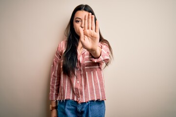 Young brunette woman wearing casual striped shirt over isolated background doing stop sing with palm of the hand. Warning expression with negative and serious gesture on the face.