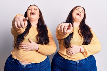 Young plus size twins wearing casual clothes laughing at you, pointing finger to the camera with...