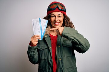 Middle age tourist woman wearing skier goggles holding airline boarding pass very happy pointing with hand and finger