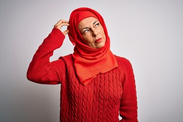 Middle age brunette woman wearing muslim traditional hijab over isolated white background confuse...