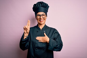 Middle age brunette chef woman wearing cooker uniform and hat over isolated pink background smiling...