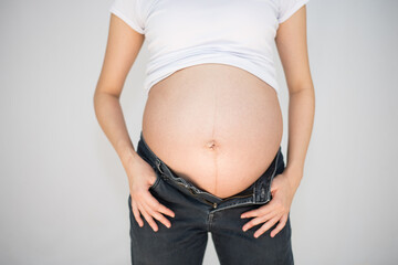 Pregnant woman trying to wear her jeans closeup
