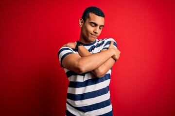 Handsome african american man wearing casual striped t-shirt standing over red background Hugging...