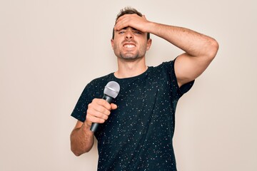 Young handsome singer man with blue eyes singing using microphone over white background stressed...