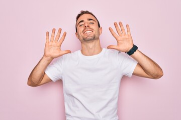 Fototapeta premium Handsome man with blue eyes wearing casual white t-shirt standing over pink background showing and pointing up with fingers number ten while smiling confident and happy.