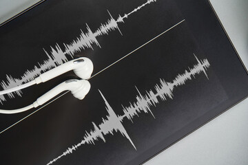 Podcast record. earbuds and sound track at tablet. Grey monochrome. Audiobook and podcasting. Audio...