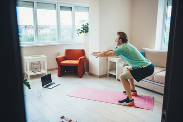 Caucasian man warming up at home while having remote lessons of fitness using a laptop