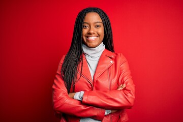 Young african american woman wearing cool fashion leather jacket over red isolated background happy face smiling with crossed arms looking at the camera. Positive person.