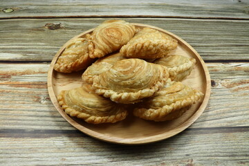 Traditional curry puff in Thai style on the wooden plate. Famous sweet and spicy snack in Asia. Fried crispy bread or bun dessert in party. Local ancient baked pie bakery.