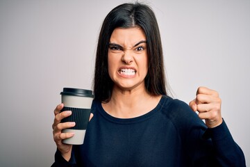 Young beautiful brunette woman drinking cup of coffee over isolated white background annoyed and frustrated shouting with anger, crazy and yelling with raised hand, anger concept