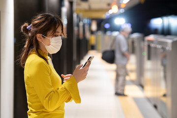 地下鉄のホームで電車を待つマスク姿の女性