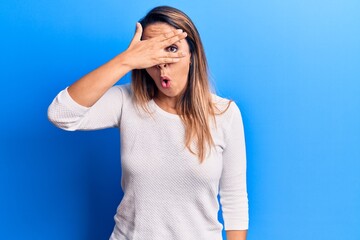 Young beautiful woman wearing casual t shirt peeking in shock covering face and eyes with hand, looking through fingers afraid