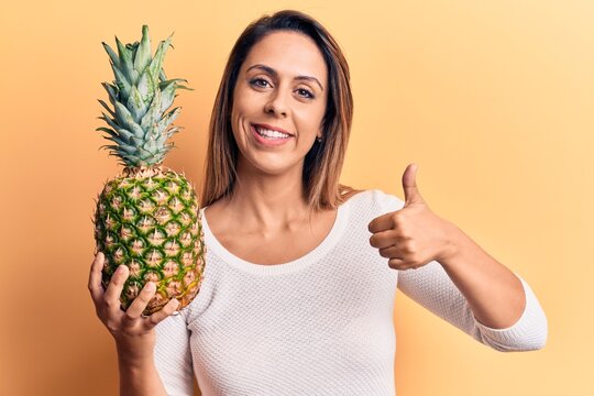 Young beautiful woman holding pineapple smiling happy and positive, thumb up doing excellent and approval sign