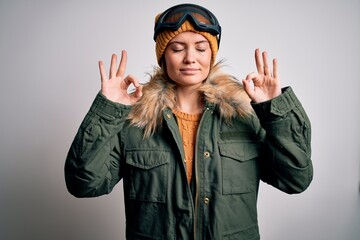 Young beautiful skier woman with blue eyes wearing snow sportswear and ski goggles relax and smiling with eyes closed doing meditation gesture with fingers. Yoga concept.