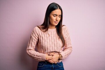 Young beautiful brunette woman wearing casual sweater over isolated pink background with hand on...