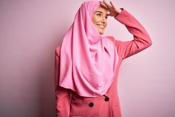 Fototapeta premium Young beautiful brunette businesswoman wearing pink muslim hijab and business jacket very happy and smiling looking far away with hand over head. Searching concept.