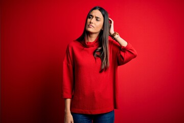 Young beautiful brunette woman wearing casual sweater over isolated red background confuse and...