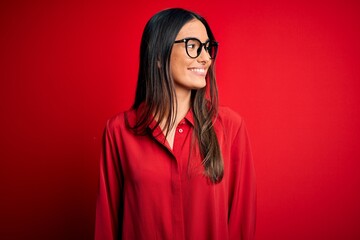 Young beautiful brunette woman wearing casual shirt and glasses over red background looking away to...
