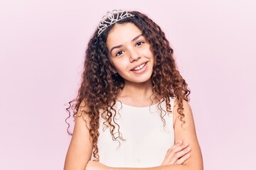 Beautiful kid girl with curly hair wearing princess tiara happy face smiling with crossed arms looking at the camera. positive person. © Krakenimages.com
