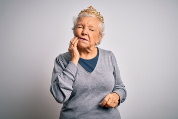 Senior beautiful grey-haired woman wearing golden queen crown over white background touching mouth with hand with painful expression because of toothache or dental illness on teeth. Dentist