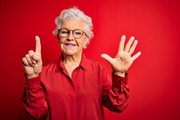 Senior beautiful grey-haired woman wearing casual shirt and glasses over red background showing and...
