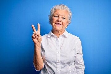 Senior beautiful woman wearing elegant shirt standing over isolated blue background showing and pointing up with fingers number two while smiling confident and happy.