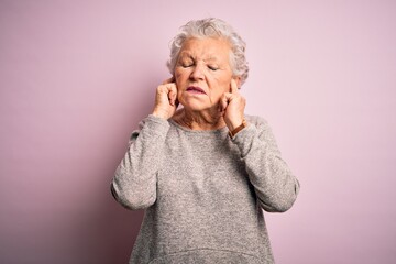 Senior beautiful woman wearing casual t-shirt standing over isolated pink background covering ears with fingers with annoyed expression for the noise of loud music. Deaf concept.