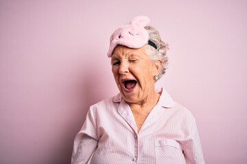 Senior beautiful woman wearing sleep mask and pajama over isolated pink background winking looking...