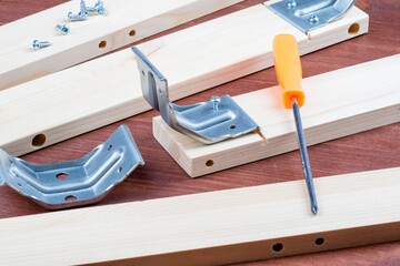 An orange screwdriver and spare parts for a wooden table lie nearby