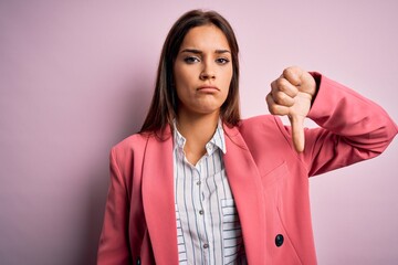 Young beautiful brunette woman wearing jacket standing over isolated pink background looking unhappy and angry showing rejection and negative with thumbs down gesture. Bad expression.