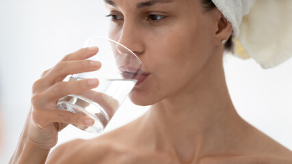 Close up beautiful woman wearing bath towel on head drinking pure still mineral water, holding...