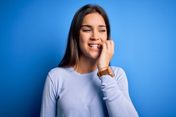 Fototapeta premium Young beautiful brunette woman wearing casual sweater standing over blue background looking stressed and nervous with hands on mouth biting nails. Anxiety problem.