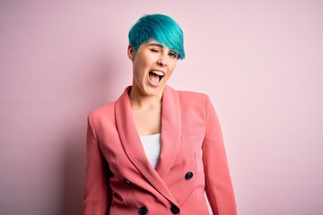 Young beautiful businesswoman with blue fashion hair wearing jacket over pink background winking looking at the camera with sexy expression, cheerful and happy face.