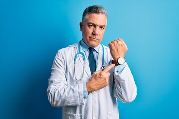 Middle age handsome grey-haired doctor man wearing coat and blue stethoscope In hurry pointing to...