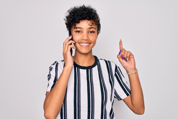 Young beautiful african american afro woman having conversation talking on the smartphone surprised with an idea or question pointing finger with happy face, number one