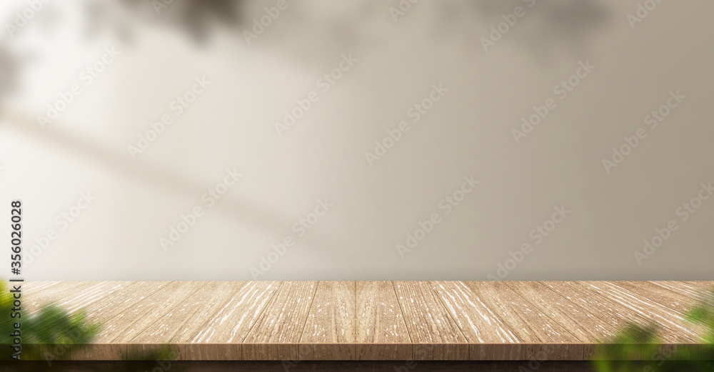 Poster wood table background with sunlight window create leaf shadow on wall with blur indoor green plant foreground.panoramic banner mockup for display of product,warm tone lights