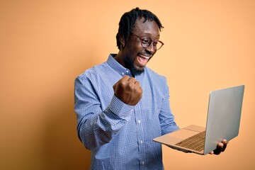 Young african american worker man working using laptop standing over yellow background screaming proud and celebrating victory and success very excited, cheering emotion