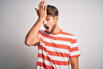 Young handsome man with beard wearing striped t-shirt standing over white background surprised with...
