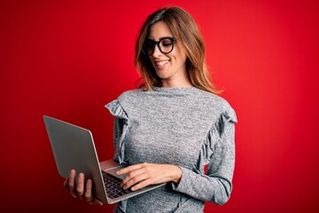 Young beautiful brunette businesswoman wearing glasses using laptop over red background with a...